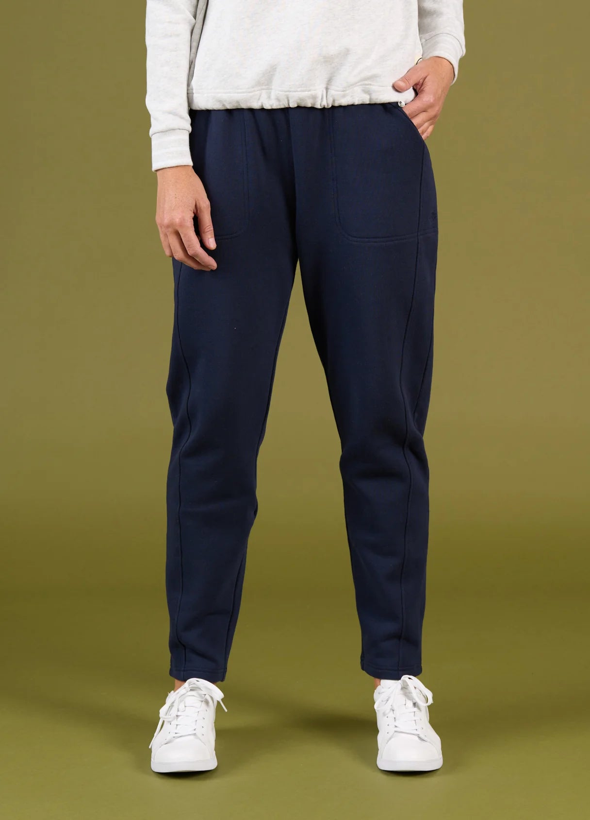 Person wearing navy jogger pants and white sneakers on a green background