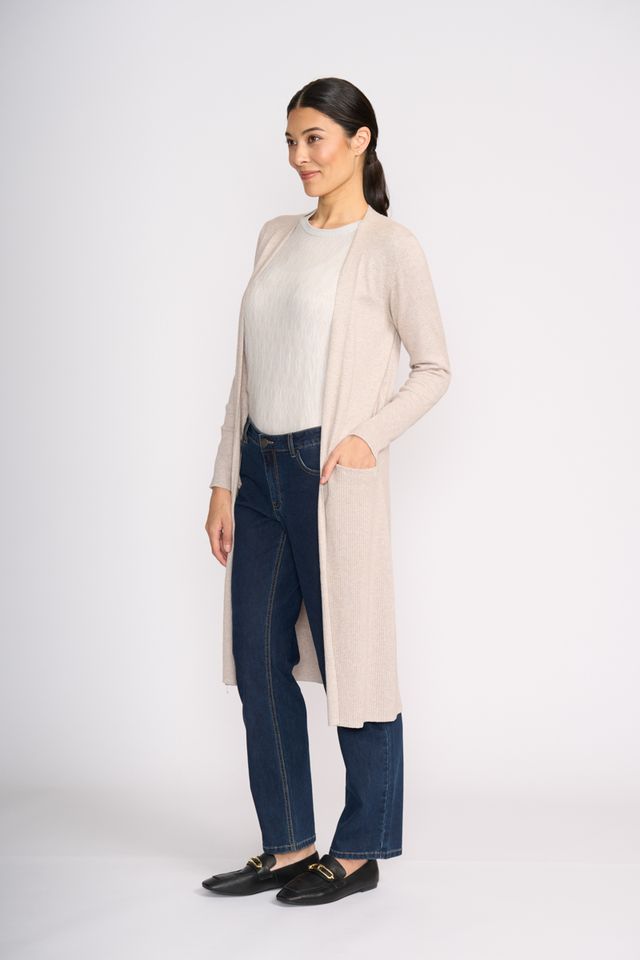 Woman wearing a beige cardigan, white shirt, and blue jeans on a white background