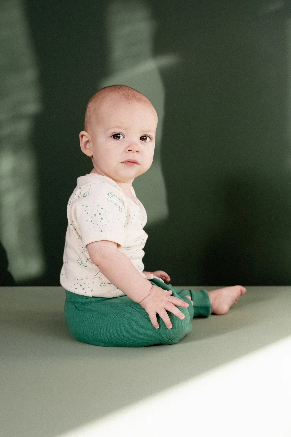 Baby sitting on a green surface with a blurred dark background