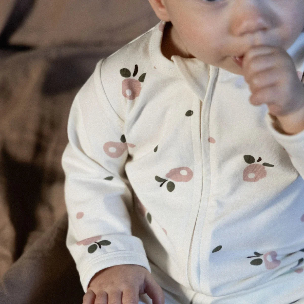 Baby wearing a white onesie with floral patterns, sitting on a brown surface.