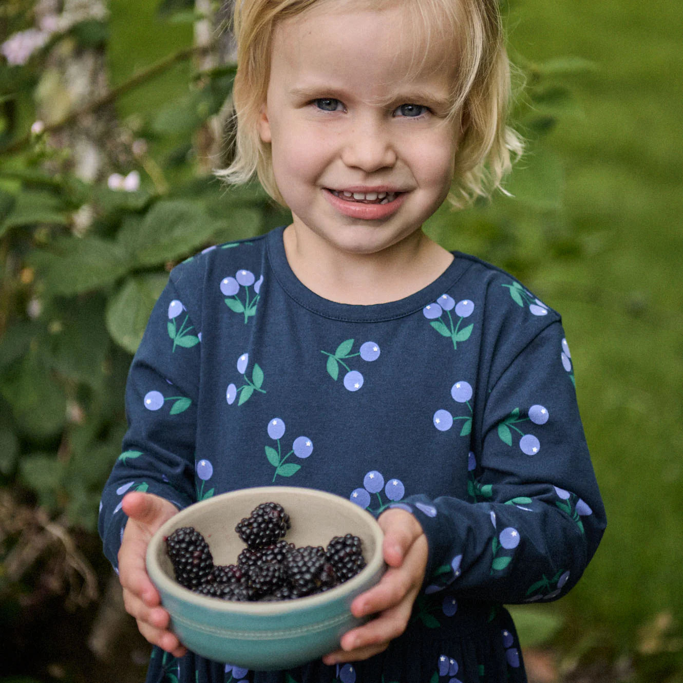 Child holding a bowl of blackberries in a garden setting