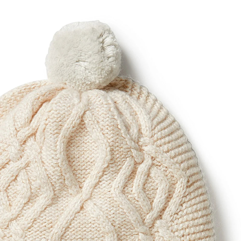 Cream-colored knitted beanie with a pom-pom on a white background