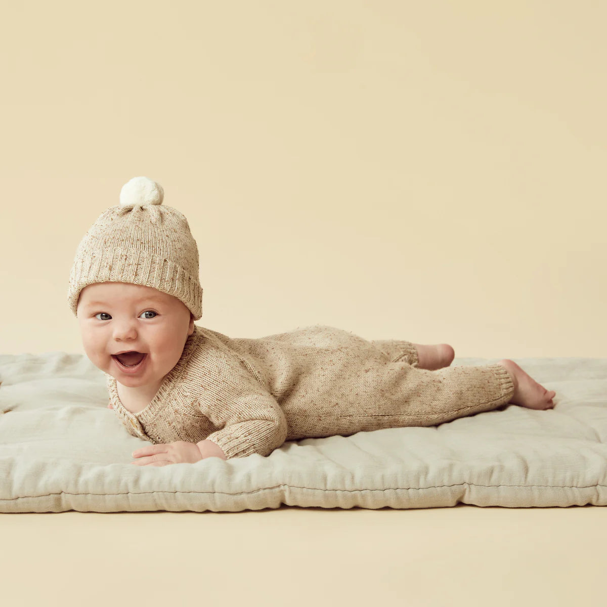 Baby wearing a beige knitted outfit and hat on a beige background