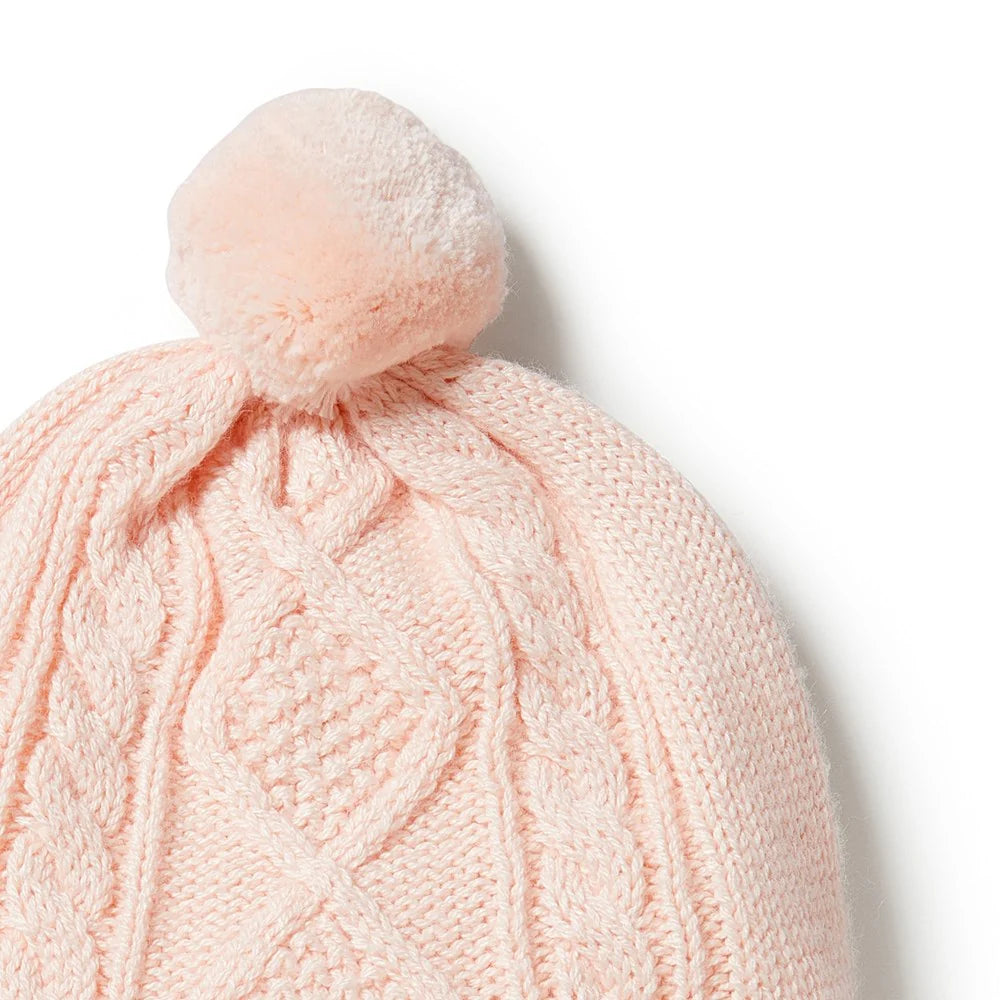 Pink knitted beanie with a pom-pom on a light gray background