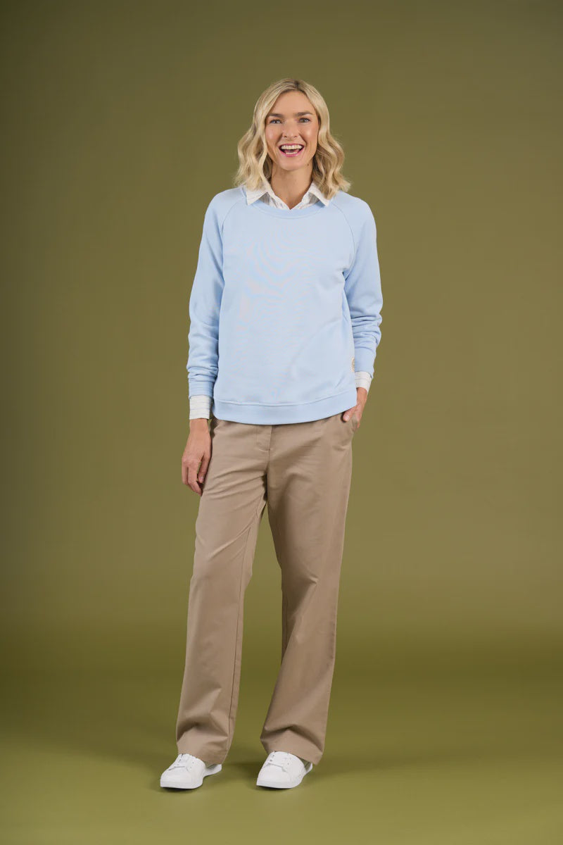Woman wearing a light blue sweater and beige pants on a green background