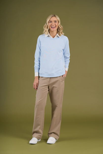 Woman wearing a light blue sweater and beige pants on a green background