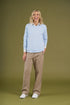 Woman wearing a light blue sweater and beige pants on a green background
