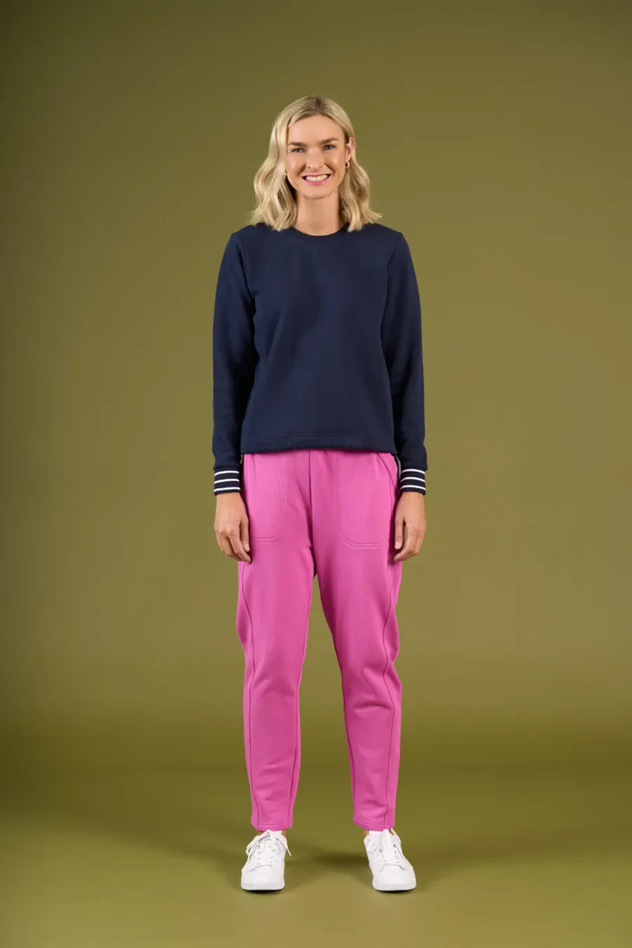 Woman wearing a navy sweater and pink pants on an olive green background