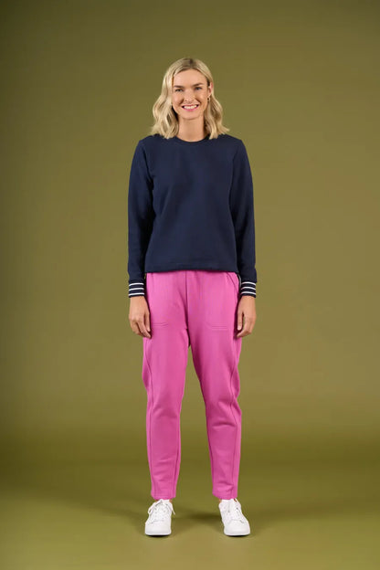 Woman wearing a navy sweater and pink pants on an olive green background