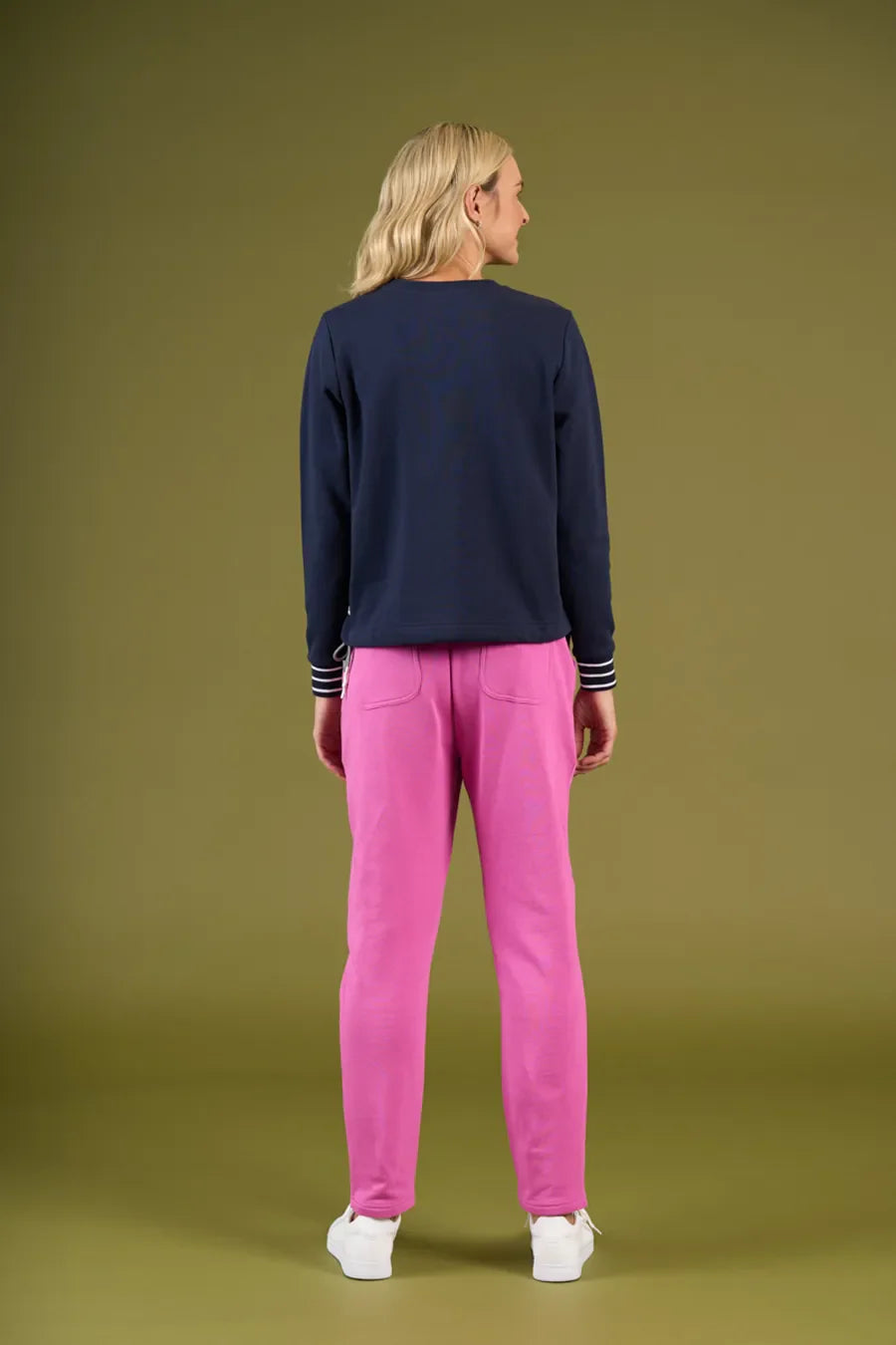 Person wearing a navy sweater and pink pants on an olive green background