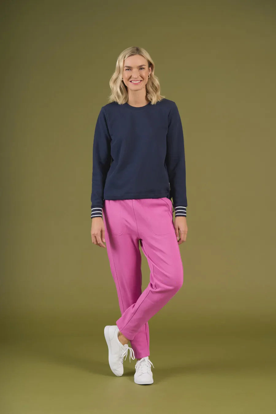 Woman wearing a navy sweater and pink pants on an olive green background
