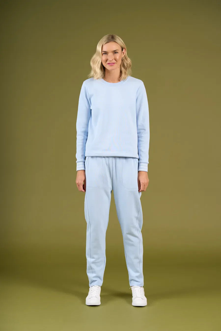 Woman wearing a light blue sweater and pants on an olive green background