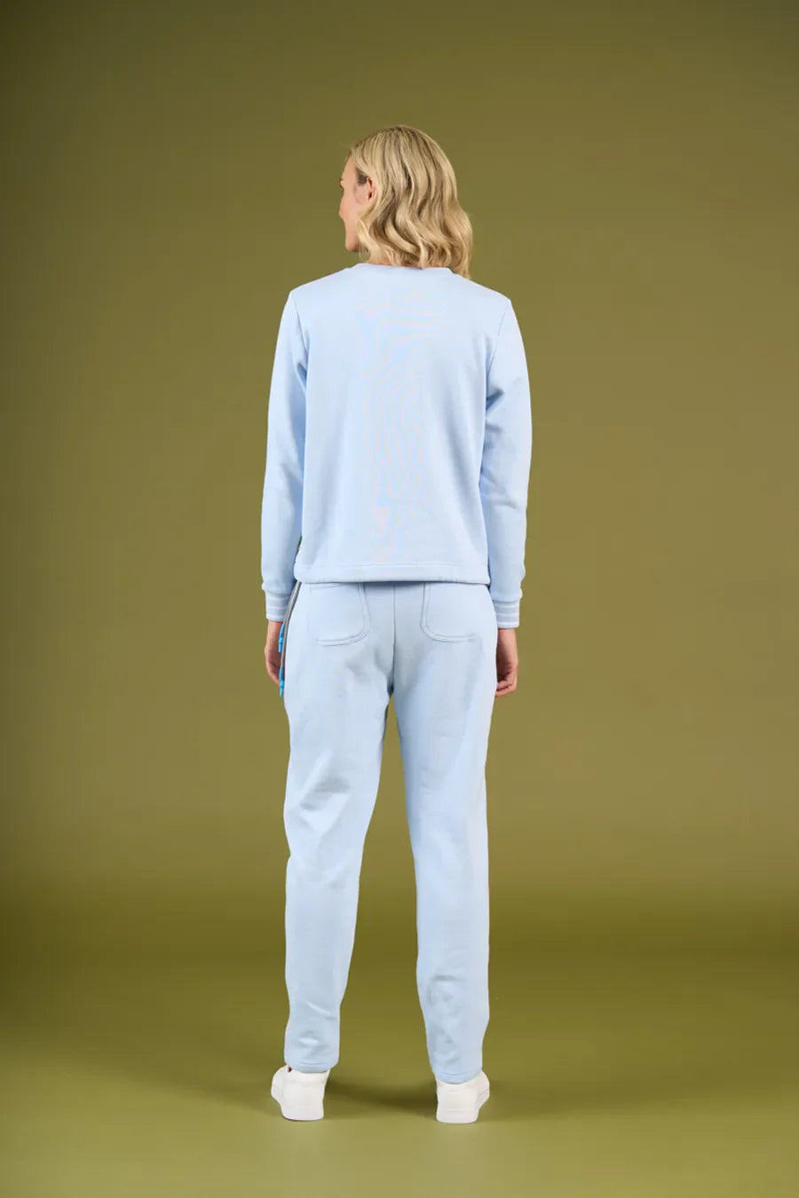 Person wearing a light blue sweater and pants on a green background