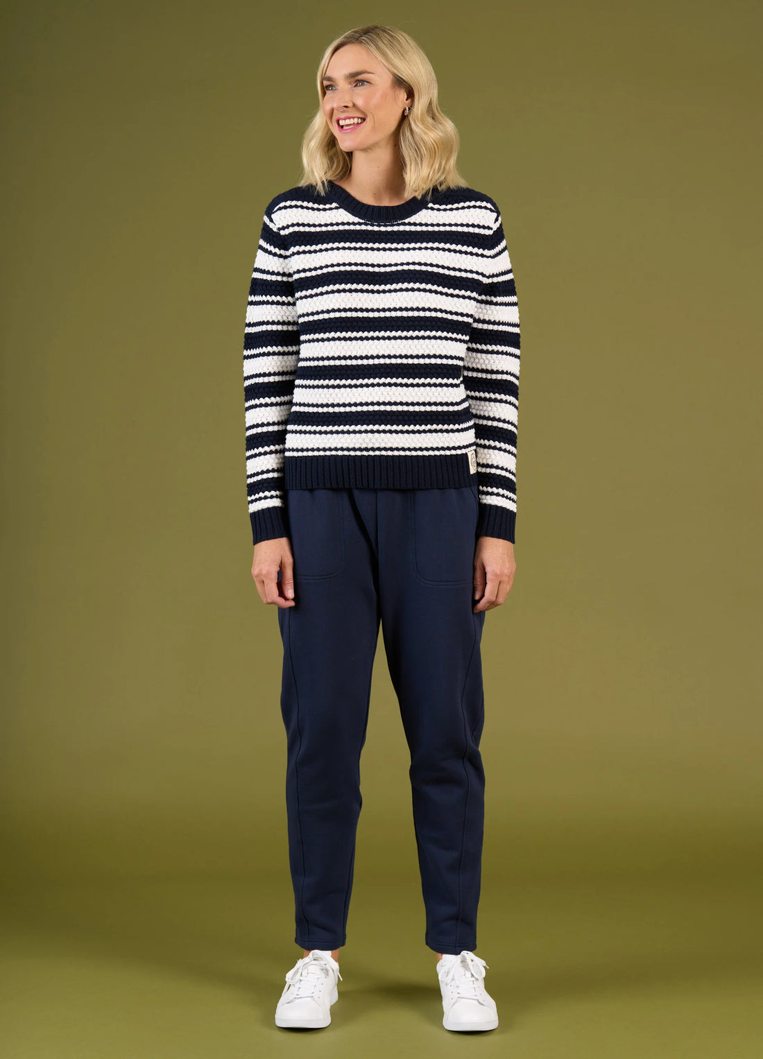 Woman wearing a black and white striped sweater and navy pants on a green background