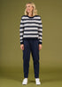 Woman wearing a black and white striped sweater and navy pants on a green background
