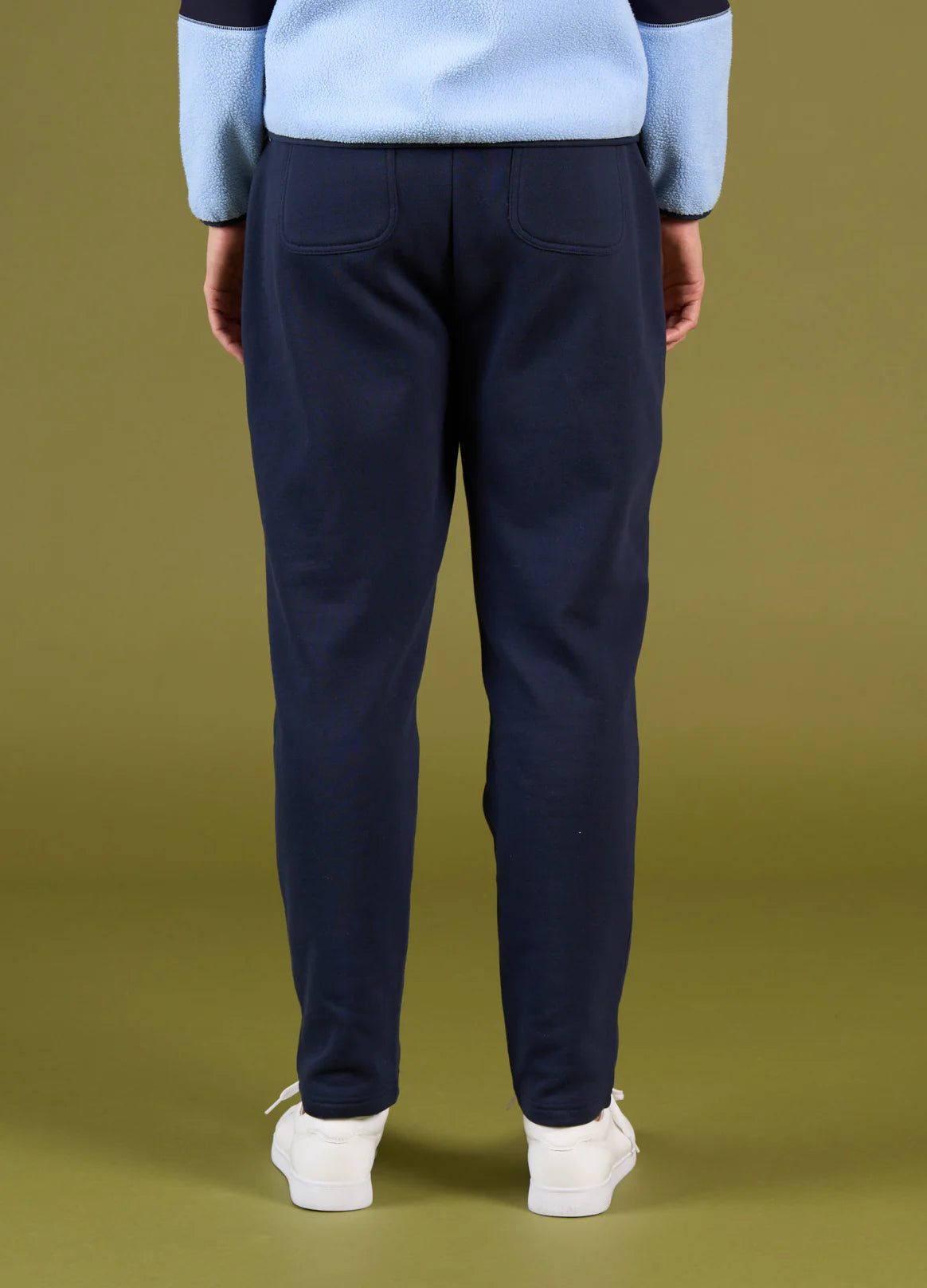 Person wearing navy pants and a light blue sweater on a green background