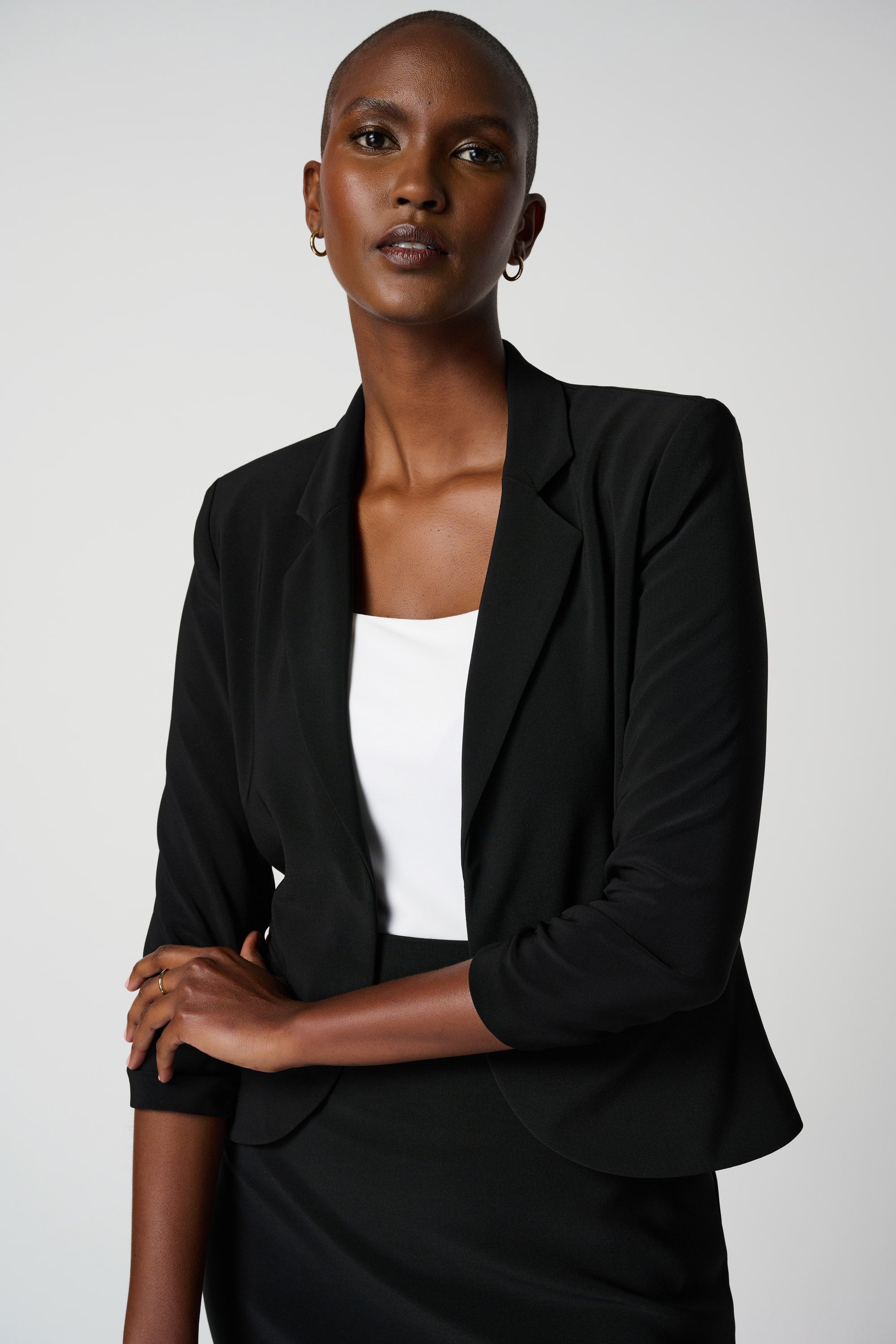A woman wearing a black classic blazer from Joseph Ribkoff with notched collar and faux front pockets, paired with a white top and a black skirt.