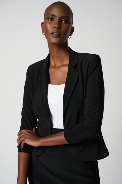 A woman wearing a black classic blazer from Joseph Ribkoff with notched collar and faux front pockets, paired with a white top and a black skirt.