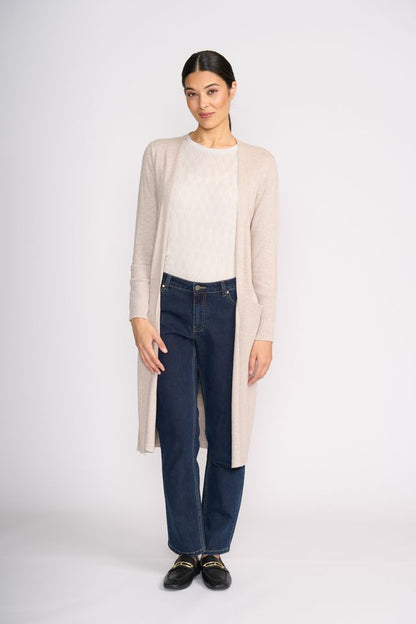 Woman wearing a beige cardigan, white shirt, and dark jeans on a white background