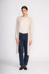 Woman wearing a beige cardigan, white shirt, and dark jeans on a white background