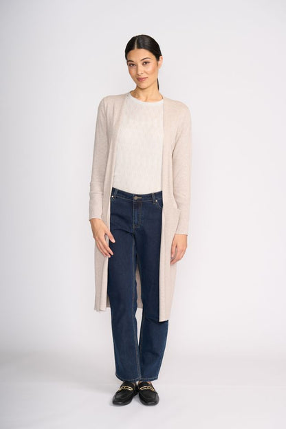 Woman wearing a beige cardigan, white sweater, dark jeans, and black shoes on a white background