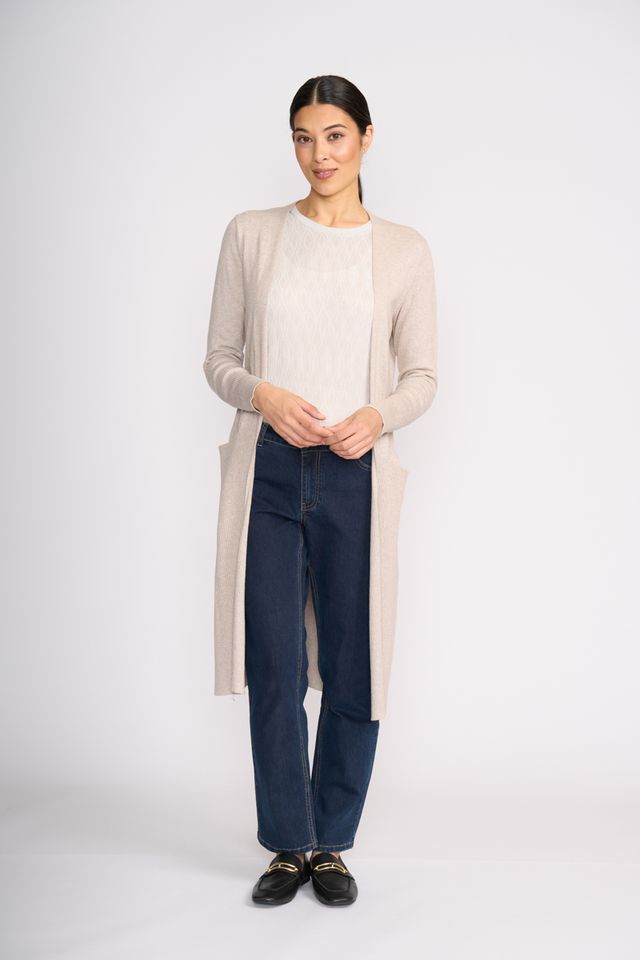 Woman wearing a beige long cardigan, white shirt, dark jeans, and black shoes on a white background
