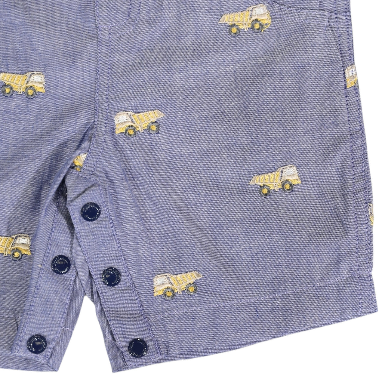 Blue denim shorts with yellow dump truck pattern and black buttons on a white background