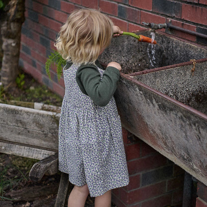 Child playing with a hose near a metal trough outdoors.