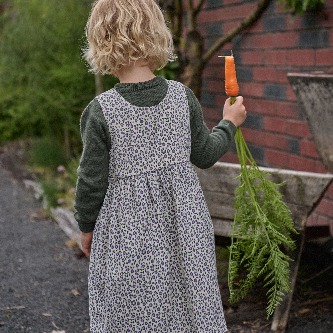 Child in a patterned dress holding a carrot outdoors.