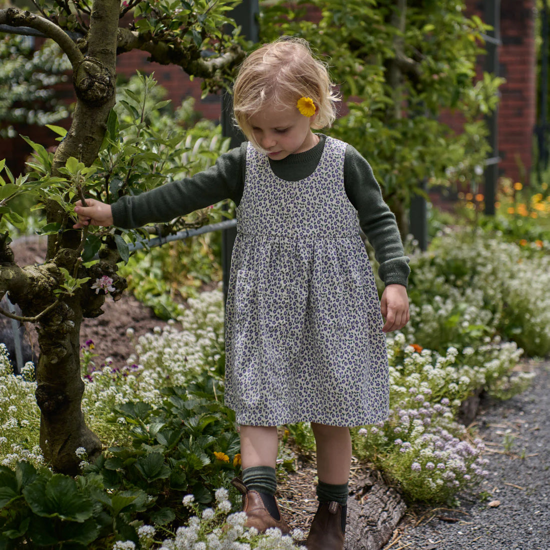 Young girl in a garden wearing a floral dress and green sweater.