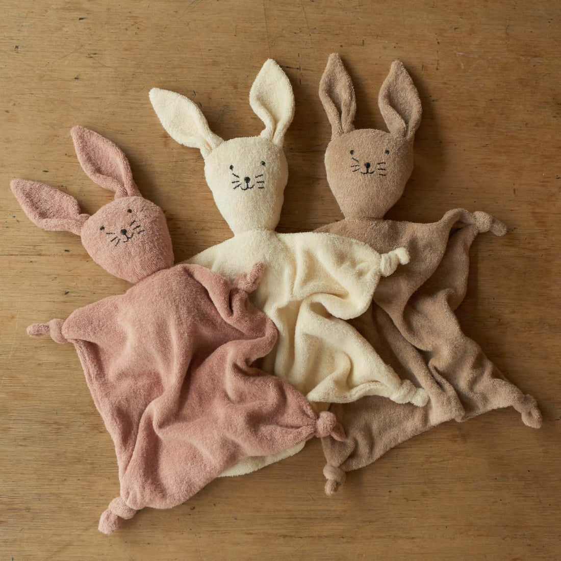 Three soft toy rabbits in different colors on a wooden surface