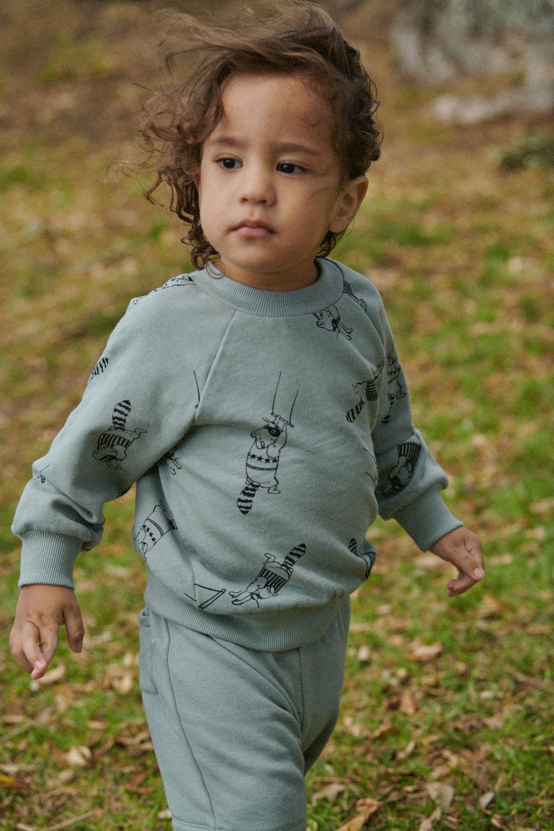 Child wearing a light green sweatshirt with animal prints outdoors on a grassy area.