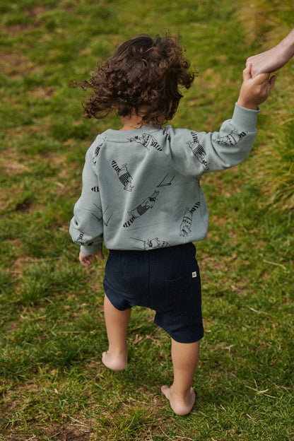 Child wearing a light green hoodie with black patterns and navy shorts standing on grass.