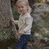 Child in a forest setting wearing a cream sweater and dark patterned pants.