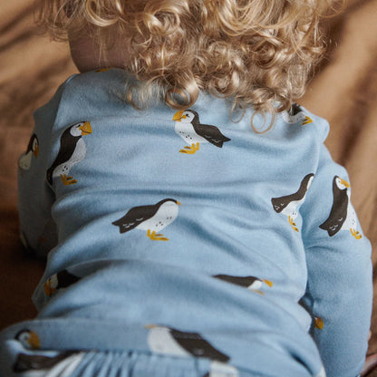 Child wearing a blue shirt with penguin pattern, sitting on a wooden floor.