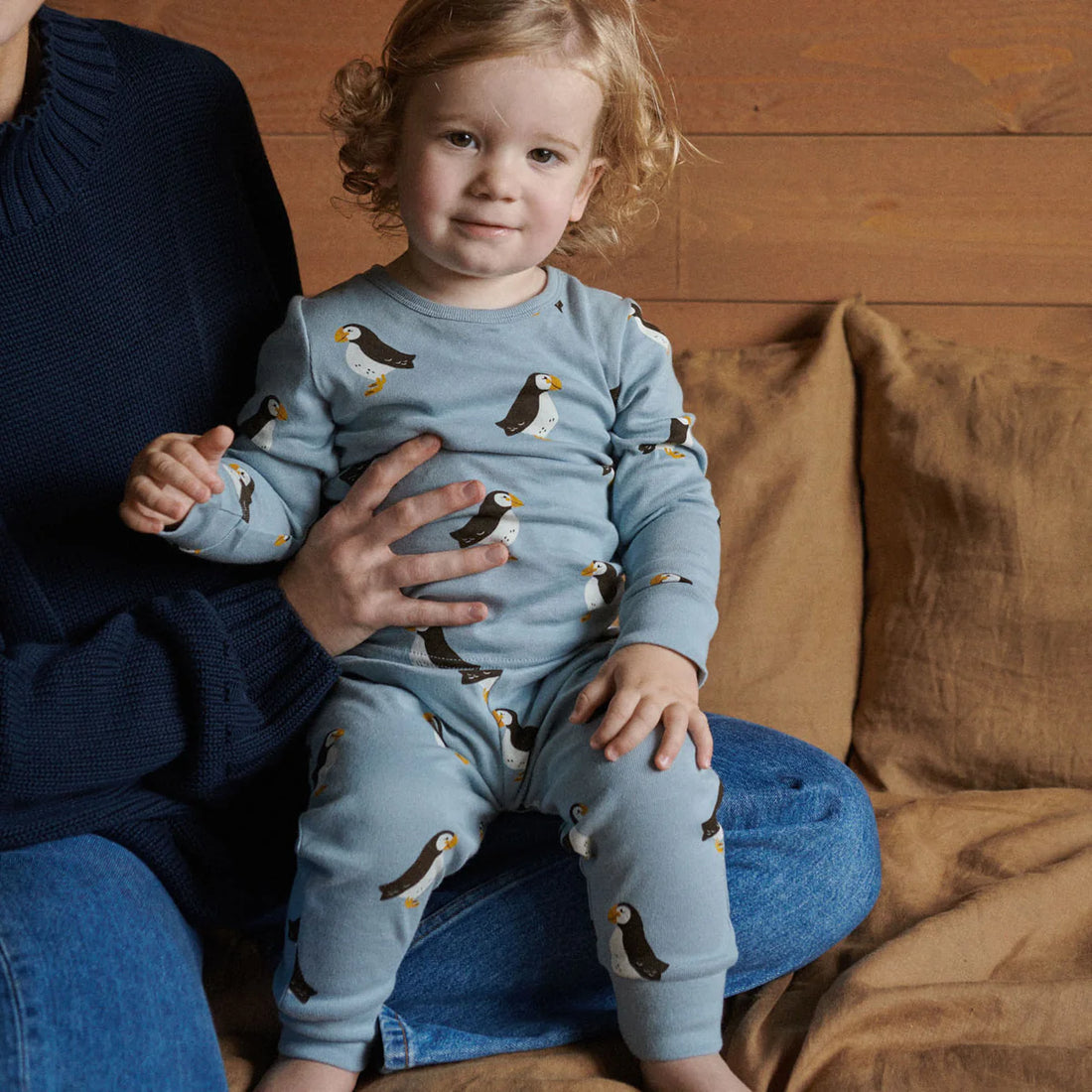 Child wearing a blue pajama set with penguin pattern, sitting on a person&