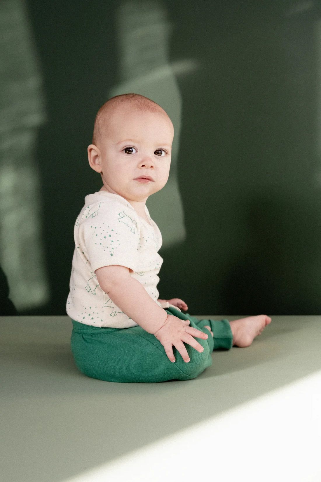 Baby sitting on a green surface with a blurred dark background
