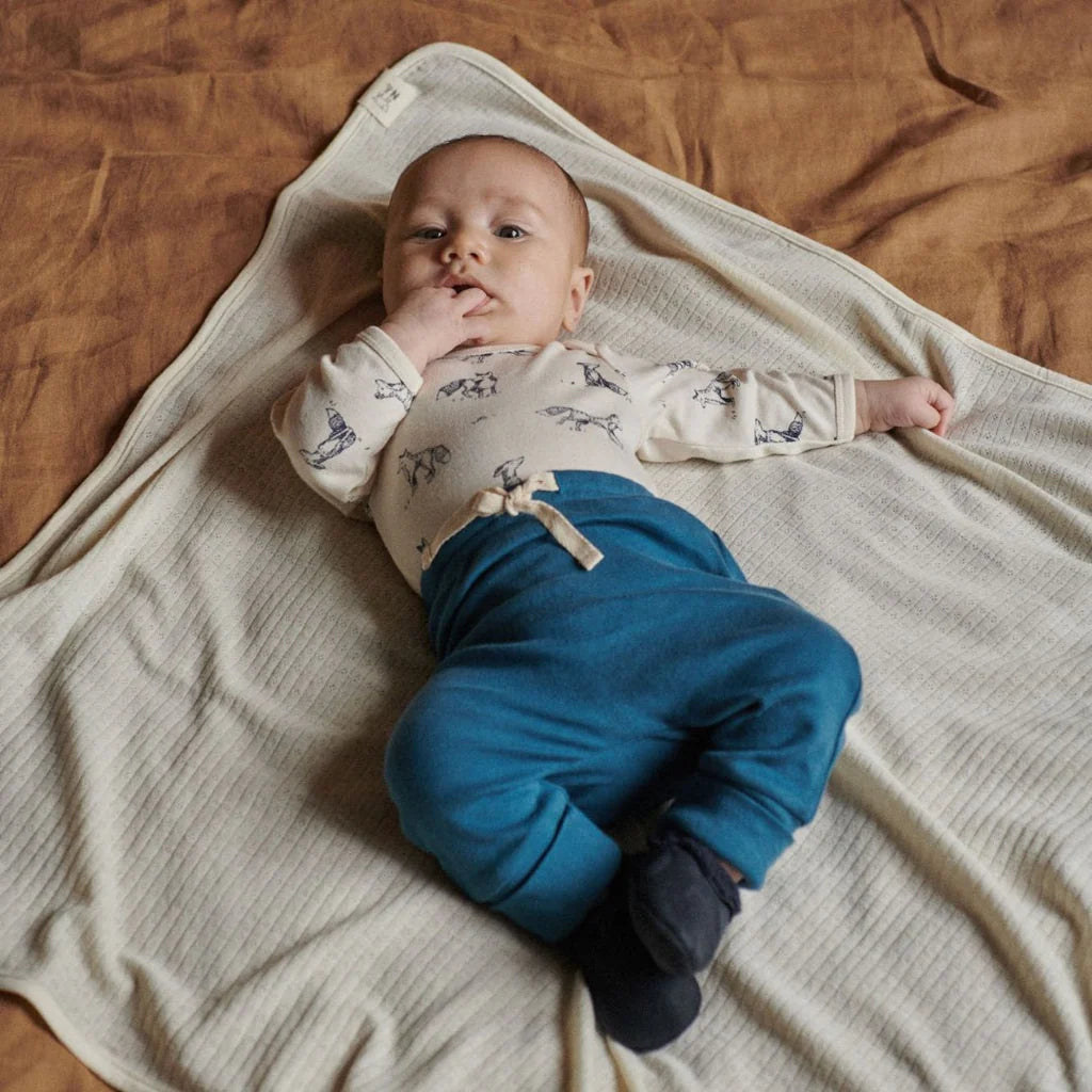 Baby lying on a blanket wearing a white shirt with blue pants