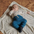 Baby lying on a blanket wearing a white shirt with blue pants