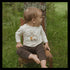 Child sitting on a wooden chair outdoors with a natural background