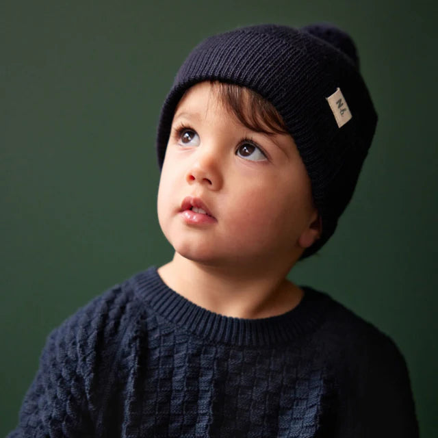 Child wearing a dark knit beanie and sweater against a green background