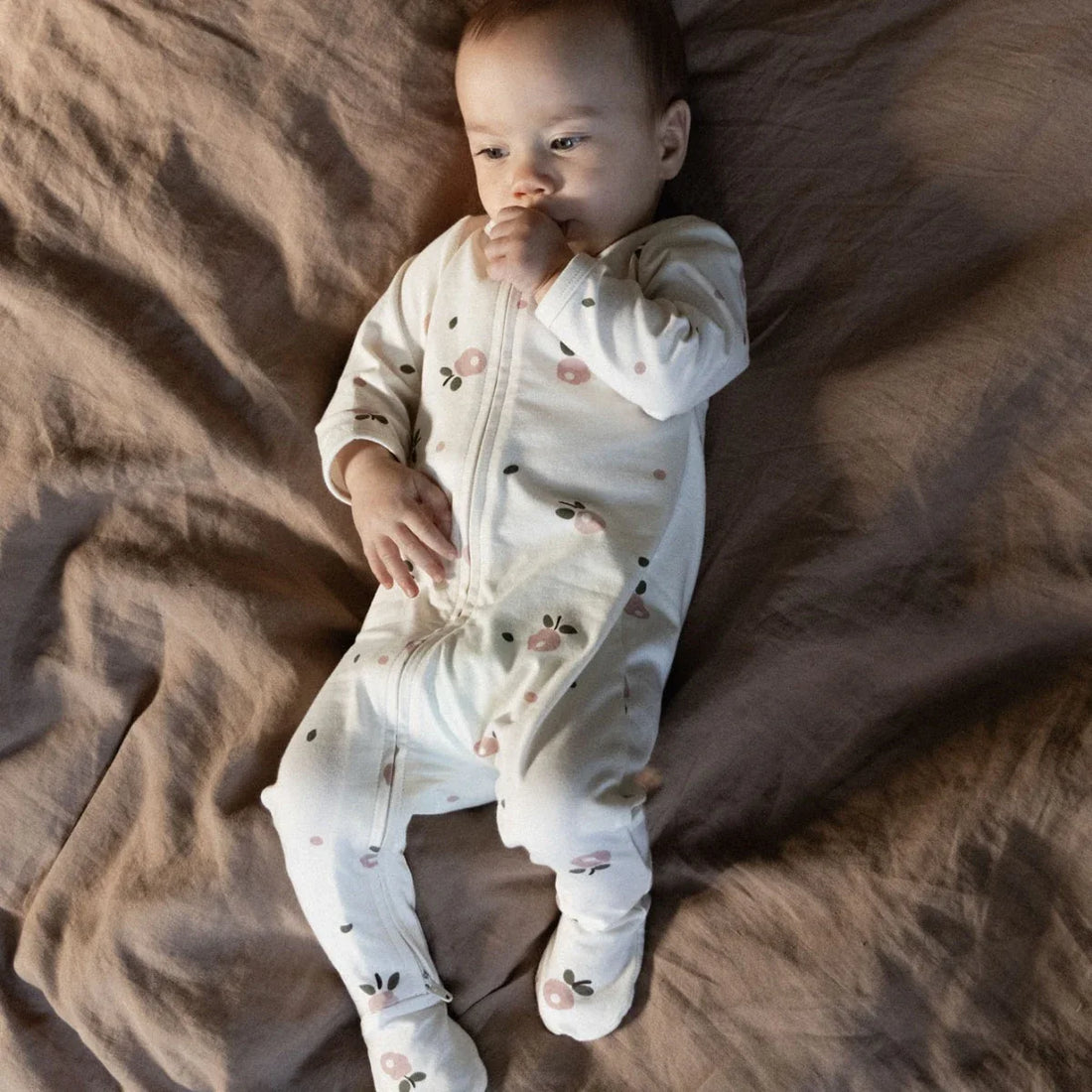Baby in a white onesie with floral patterns lying on a brown blanket