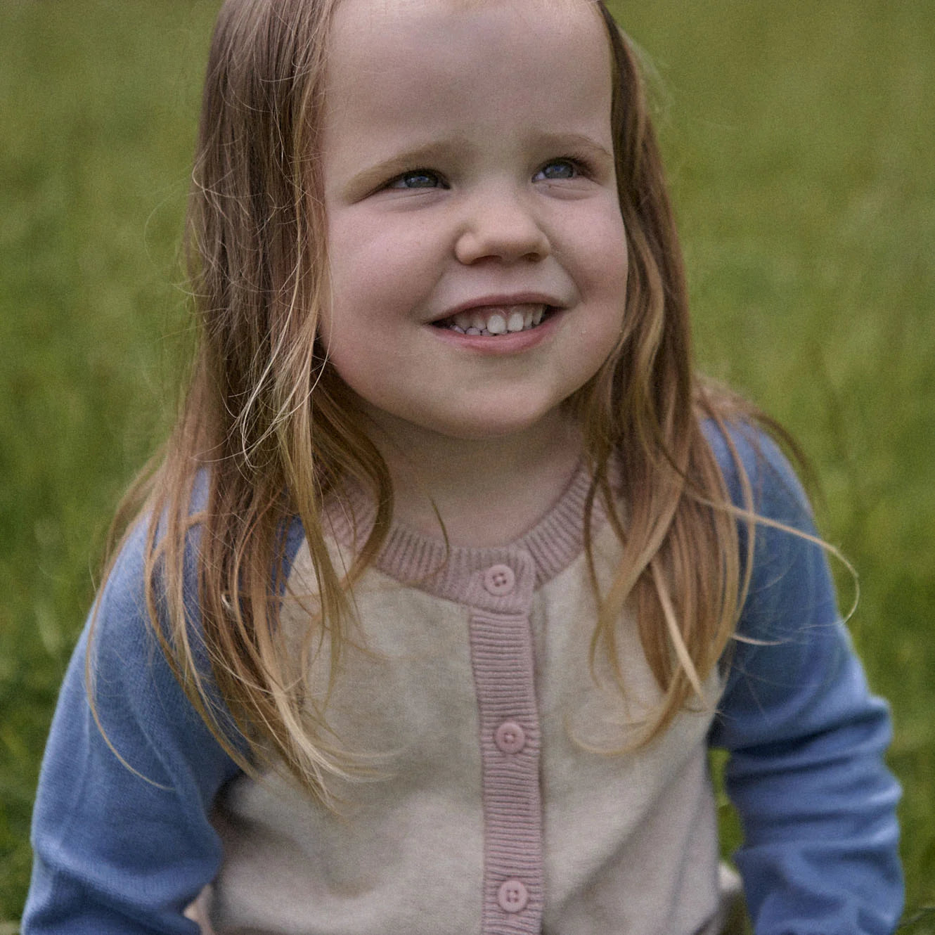 Young girl with a blue sweater and pink cardigan standing in a grassy field