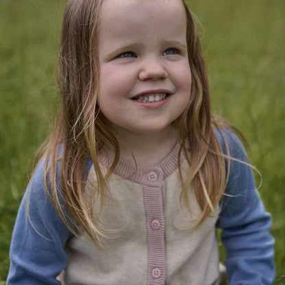 Young girl with a blue sweater and pink cardigan standing in a grassy field