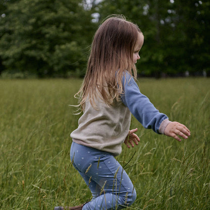 Child running through a grassy field with trees in the background