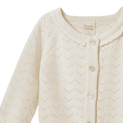 Close-up of a cream-colored baby cardigan with a patterned texture on a white background.