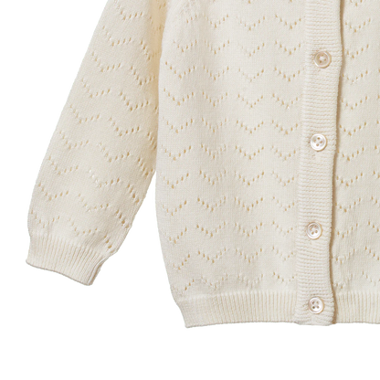 Close-up of a cream-colored cardigan with button details on a white background