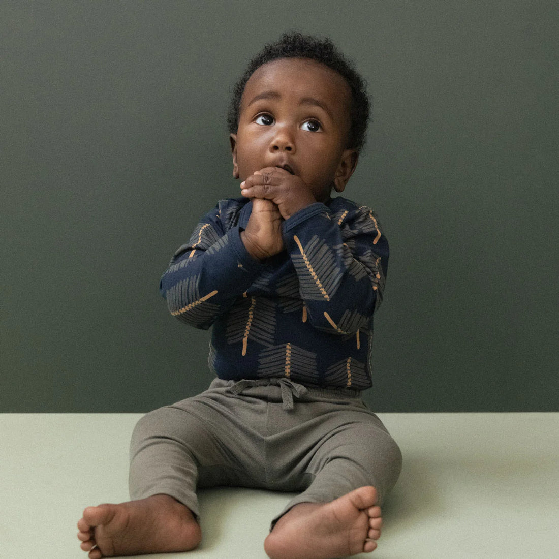 Child sitting on a light surface with a dark green background