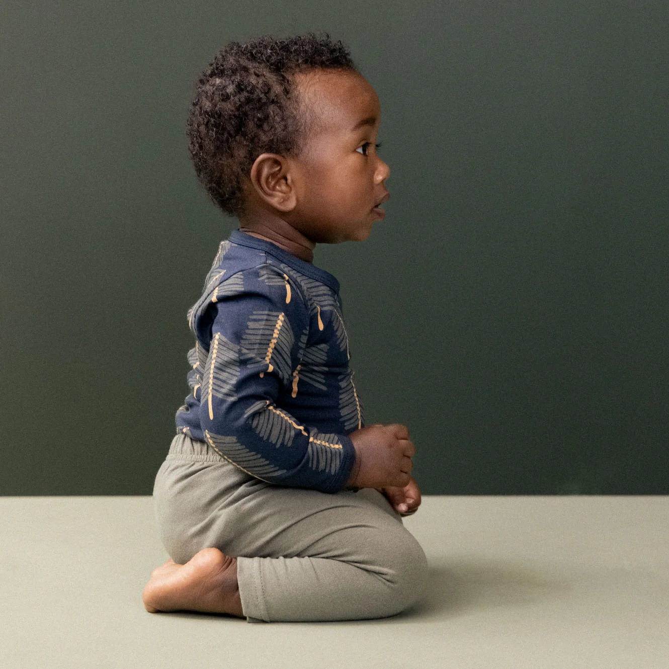 Child sitting on a plain surface with a dark green background