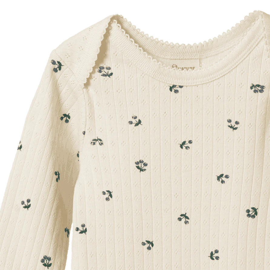 Close-up of a cream-colored sweater with small green floral patterns on a white background.